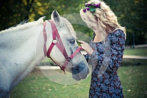 Young boho style woman pat horse in park summer day