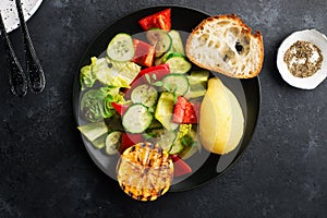 Young boiled potatoes, salad of leafy greens, cucumber, capsicum, micro greens, oil, with lemon on a dark background in