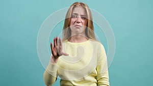 Young bored woman make blah blah gesture with hand, on turquoise background.