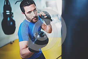 Young boxer doing some training on punching bag at gym. Bearded caucasian boxer training with punching bag in gym