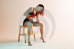 A young boxer girl with red bandages on her hands poses on a chair in a photo Studio.