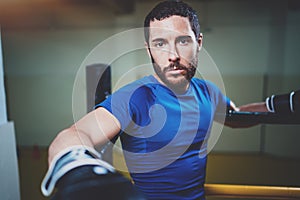 Young boxing man ready to muay thai fight on ring.Bearded athlete in black gloves looking at the camera.Blurred