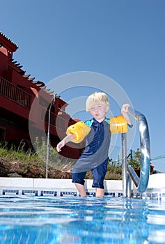 Young boy with arm bands climbing into swimming pool