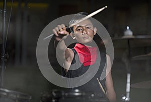 Young boy as talented rock band drummer . portrait on stage of handsome and cool Asian American teenager playing drum kit