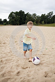 A young boy on the beach runs towards a soccer ball and wants to score a goal