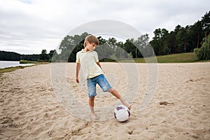 A young boy on the beach runs towards a soccer ball and wants to score a goal