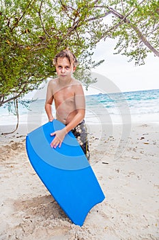 Young boy at the beach with surf board looks exhausted
