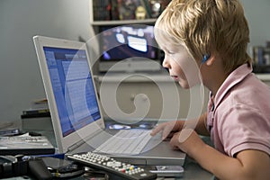 Young boy in bedroom using laptop and listening to