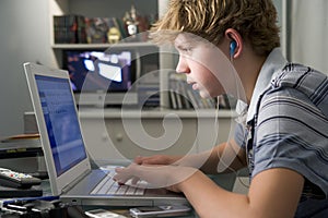 Young boy in bedroom using laptop listening to mp3 photo