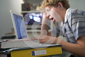 Young boy in bedroom yawning using laptop