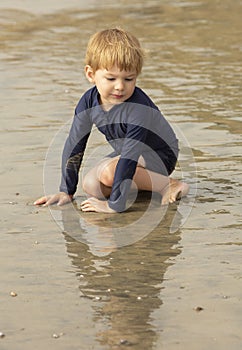 Young boy with blonde hair and navy swimsuit having fun splashing at the beach