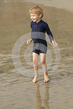 Young boy with blonde hair and navy swimsuit having fun splashing at the beach