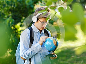 Young boy in blue shirt and round glasses looks and points on globe in his hands. Education, back to school