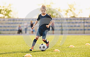 Young boy in blue soccer jersey uniform running after ball on training pitch