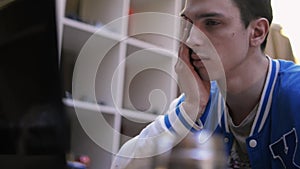 Young boy in blue sport jacket yawning in front screen of computer in room. Sleepy. Tiredness