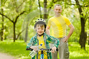 Young boy with a bottle of water is learning to ride a bike with his grandfather