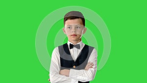 Young boy in bow tie and vest with crossed arms nodding his head while looking at camera and saying something on a Green