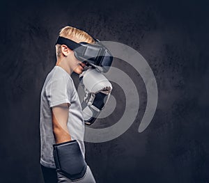 Schoolboy boxer with blonde hair dressed in a white t-shirt wearing visual reality glasses and boxing gloves, workout in