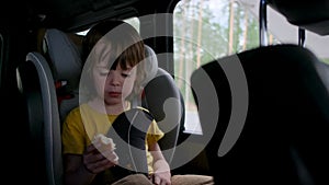 Young boy with brown hair eats toasty bun in car seat