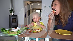 Young boy and brunette mom sitting at a table and eating hamburgers