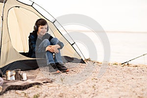 Young boy on camping trip.Child in a tent on beach listening music. Camping. Happy teen at spring vacations.