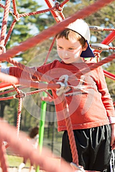 Young boy child playing at outdoor playground climbing net