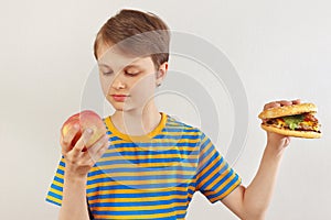 Young boy chooses between fastfood and fruit on white background