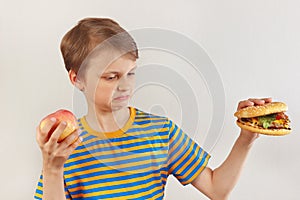 Young boy chooses between fastfood and healthy diet on white background