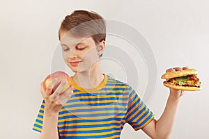 Young boy chooses between hamburger and healthy diet on white background