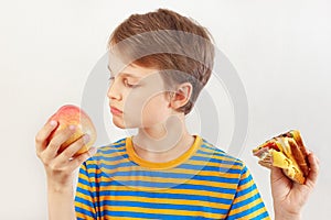 Young boy chooses between sandwich and apple on white background