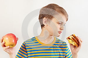 Young boy chooses between sandwich and fruit on white background