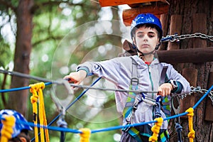 Young boy climbing pass obstacles in rope. Child in forest adventure park