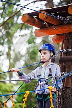 Young boy climbing pass obstacles in rope. Child in forest adventure park