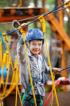 Young boy climbing pass obstacles in rope. Child in forest adventure park