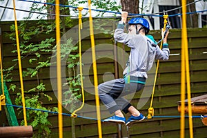 Young boy climbing pass obstacles in rope. Child in forest adventure park