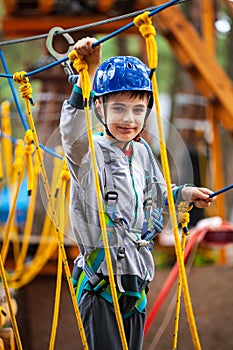 Young boy climbing pass obstacles in rope. Child in forest adventure park