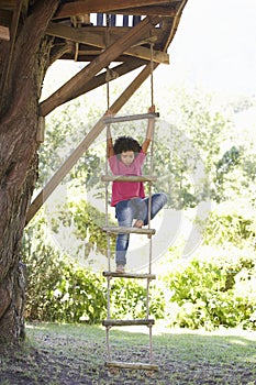 Young Boy Climbing Rope Ladder To Treehouse