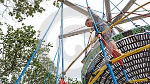 Young boy climbing up a playground climbing frame rope ladder