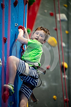 Young boy climbing up on practice wall in indoor rock gym