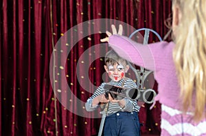 Young Boy Clown Aiming Large Gun at Blond Girl