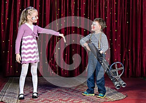 Young Boy Clown Aiming Large Gun at Blond Girl