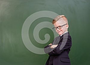 Young boy with crossed arms standing near chalkboard