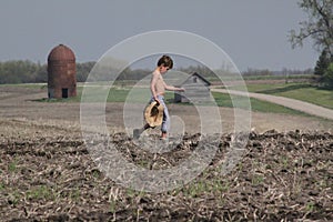 Young boy crosses field carrying straw hat