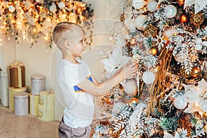 Young boy decorating Christmas tree on Christmas eve at home. Young kid in light bedroom with winter decoration. Happy family at