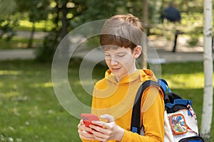 Young boy with dressed yellow hoodie looking at his mobile phone, outdoors spring time.