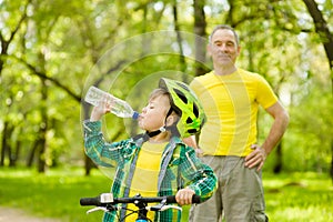 Young boy drink water is learning to ride a bike with his grandfather