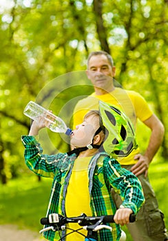 Young boy drink water is learning to ride a bike with his grandfather