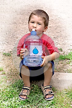 Young boy drinking from a large jug of water after outdoor activity