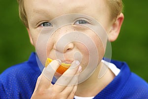 Young boy eating an orange outside