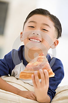 Young boy eating pizza slice in living room